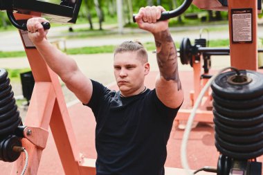 Beyaz erkek sporcu, kollarını ve göğsünü spor aletleri ile eğitiyor, yaz parkında spor yapıyor.