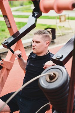 Beyaz erkek sporcu, kollarını ve göğsünü spor aletleri ile eğitiyor, yaz parkında spor yapıyor.