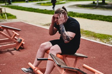 Beyaz erkek sporcu, karın kaslarını bir sokak egzersiz makinesinde şişiriyor, yaz parkında egzersiz yapıyor.