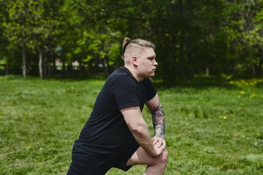 Beyaz erkek sporcu yaz parkında antrenman yapmadan önce ısınma egzersizi yapıyor.