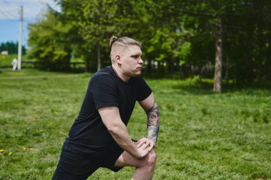 Beyaz erkek sporcu yaz parkında antrenman yapmadan önce ısınma egzersizi yapıyor.