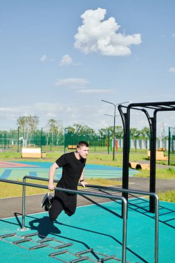 Beyaz tenli erkek sporcu, yaz parkında barfiks çekiyor.