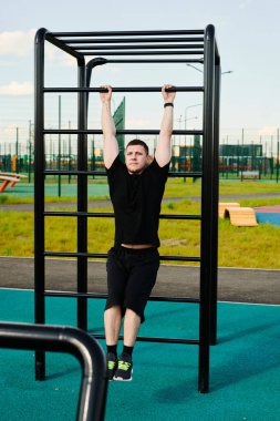 Beyaz tenli erkek sporcu, yaz parkında barfiks çekiyor.