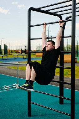 Beyaz tenli erkek sporcu, yaz parkında barfiks çekiyor.