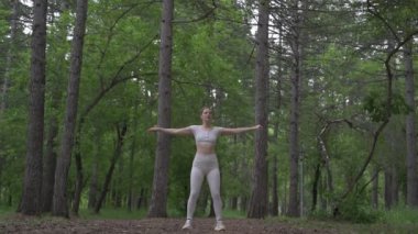 Beyaz takım elbiseli beyaz kadın yeşil orman parkında egzersiz yapıyor. Açık hava egzersizi.