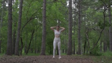 Beyaz takım elbiseli beyaz kadın yeşil orman parkında egzersiz yapıyor. Açık hava egzersizi.