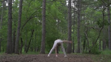 Beyaz takım elbiseli beyaz kadın yeşil orman parkında egzersiz yapıyor. Açık hava egzersizi.