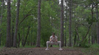 Beyaz takım elbiseli beyaz kadın yeşil orman parkında egzersiz yapıyor. Açık hava egzersizi.