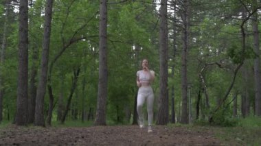 Beyaz takım elbiseli beyaz kadın yeşil orman parkında egzersiz yapıyor. Açık hava egzersizi.