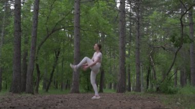 Beyaz takım elbiseli beyaz kadın yeşil orman parkında egzersiz yapıyor. Açık hava egzersizi.