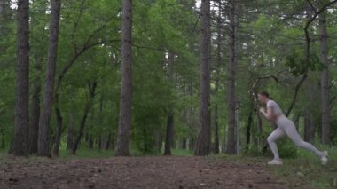Beyaz takım elbiseli beyaz kadın yeşil orman parkında egzersiz yapıyor. Açık hava egzersizi.