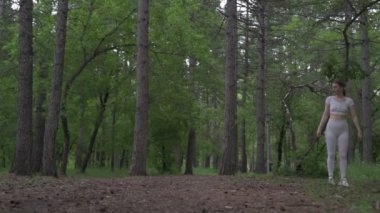 Beyaz takım elbiseli beyaz kadın yeşil orman parkında egzersiz yapıyor. Açık hava egzersizi.