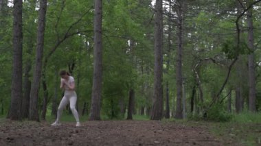 Beyaz takım elbiseli beyaz kadın yeşil orman parkında egzersiz yapıyor. Açık hava egzersizi.