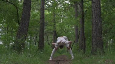Beyaz takım elbiseli beyaz kadın yeşil orman parkında egzersiz yapıyor. Açık hava egzersizi.