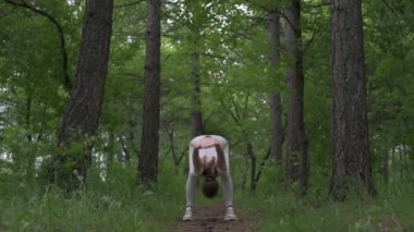 Beyaz takım elbiseli beyaz kadın yeşil orman parkında egzersiz yapıyor. Açık hava egzersizi.