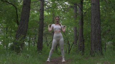Beyaz takım elbiseli beyaz kadın yeşil orman parkında egzersiz yapıyor. Açık hava egzersizi.