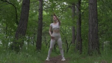 Beyaz takım elbiseli beyaz kadın yeşil orman parkında egzersiz yapıyor. Açık hava egzersizi.