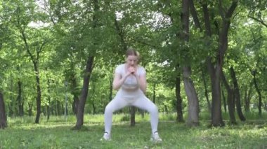 Beyaz takım elbiseli beyaz kadın yeşil orman parkında egzersiz yapıyor. Açık hava egzersizi.
