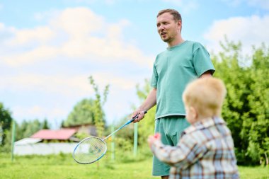 Mutlu aile yaz parkında yeşil çimlerde badminton oynuyor.