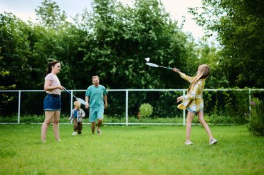 Mutlu aile yaz parkında yeşil çimlerde badminton oynuyor.