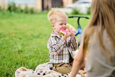 Mutlu Kafkas ailesi piknikte yeşil çimenlerin üzerinde oturmuş karpuz yiyor ve eğleniyorlar.