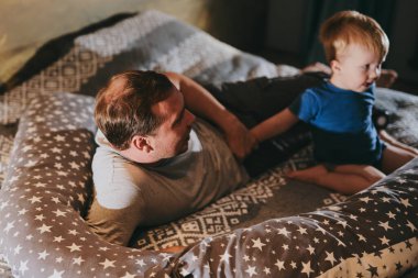 Baba ve küçük oğlu rahat bir yatakta uzanıp TV 'de film izliyorlar. Mutlu aile evde birlikte vakit geçiriyor.