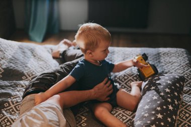 Baba ve küçük oğlu rahat bir yatakta uzanıp TV 'de film izliyorlar. Mutlu aile evde birlikte vakit geçiriyor.