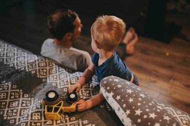 Baba ve küçük oğlu rahat bir yatakta uzanıp TV 'de film izliyorlar. Mutlu aile evde birlikte vakit geçiriyor.