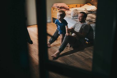 Baba ve küçük oğlu rahat bir yatakta uzanıp TV 'de film izliyorlar. Mutlu aile evde birlikte vakit geçiriyor.