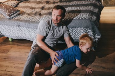 Baba ve küçük oğlu rahat bir yatakta uzanıp TV 'de film izliyorlar. Mutlu aile evde birlikte vakit geçiriyor.