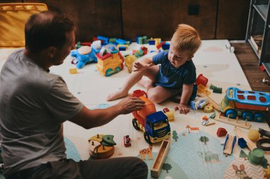 Babasıyla evde oyuncaklarla oynayan küçük bir çocuk. Mutlu baba ve oğul birlikte vakit geçiriyorlar.