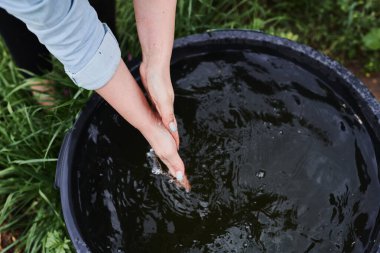 Bahçesinde bir kadın çalışıyor, çiçekleri sulayıp otları temizliyor.