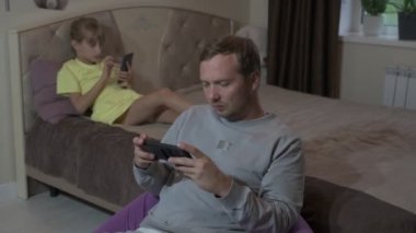 Baba ve kızı evde oturup cep telefonuyla oyun oynuyorlar.