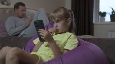 Baba ve kızı evde oturup cep telefonuyla oyun oynuyorlar.