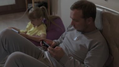Baba ve kızı evde oturup cep telefonuyla oyun oynuyorlar.