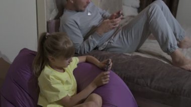 Baba ve kızı evde oturup cep telefonuyla oyun oynuyorlar.