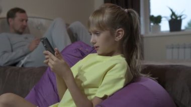 Baba ve kızı evde oturup cep telefonuyla oyun oynuyorlar.