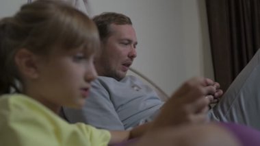 Baba ve kızı evde oturup cep telefonuyla oyun oynuyorlar.