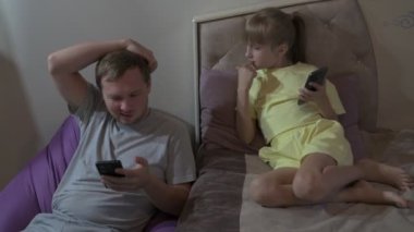 Baba ve kızı evde oturup cep telefonuyla oyun oynuyorlar.