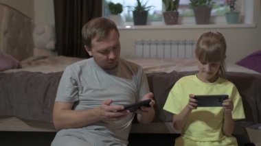Baba ve kızı evde oturup cep telefonuyla oyun oynuyorlar.
