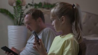 Baba ve kızı evde oturup cep telefonuyla oyun oynuyorlar.