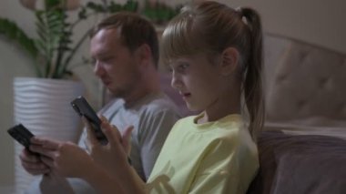 Baba ve kızı evde oturup cep telefonuyla oyun oynuyorlar.