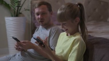 Baba ve kızı evde oturup cep telefonuyla oyun oynuyorlar.