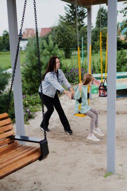 Anne kızını çocuk parkında salıncakta sallıyor. Mutlu çocukluk, hafta sonları eğlenmek.