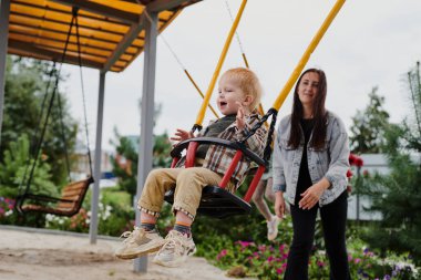 Anne oğlunu oyun parkında salıncakta sallıyor. Mutlu çocukluk, hafta sonları eğlenmek.