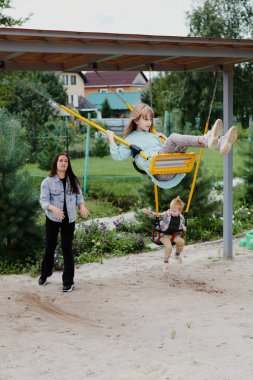 Anne kızını çocuk parkında salıncakta sallıyor. Mutlu çocukluk, hafta sonları eğlenmek.