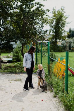 Anne ve oğlu parkta bir kediyle oynuyorlar. Mutlu çocukluk, hafta sonları eğlenmek.
