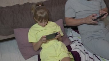 Baba ve kızı evde oturup cep telefonuyla oyun oynuyorlar.
