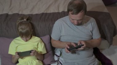 Baba ve kızı evde oturup cep telefonuyla oyun oynuyorlar.
