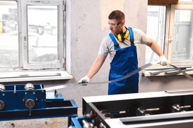 Mavi üniformalı profesyonel mühendis fabrikada çalışıyor. Yuvarlak metal, metal işleme ve metal çit üretimi